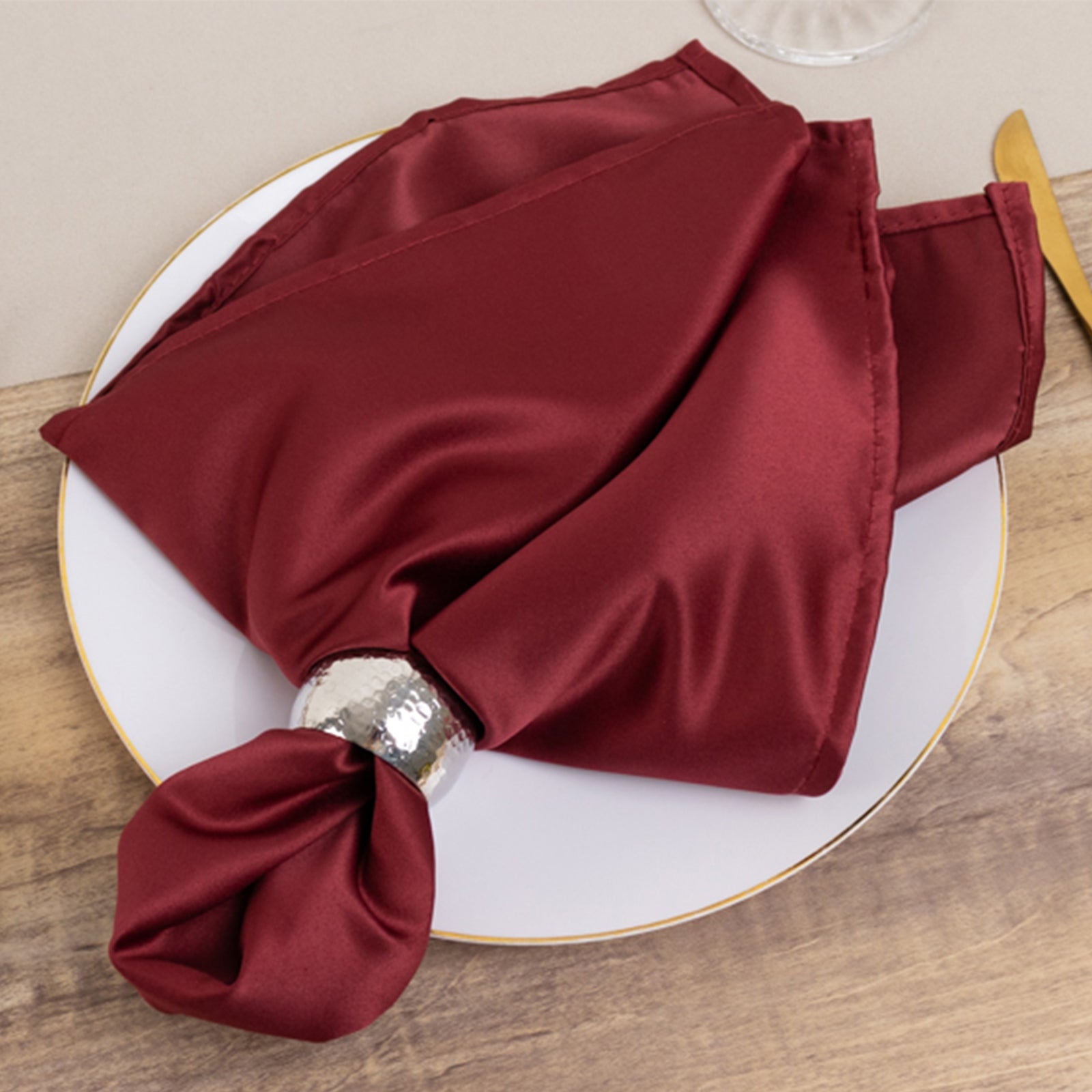 Burgundy satin napkin on a plate with a silver ring.