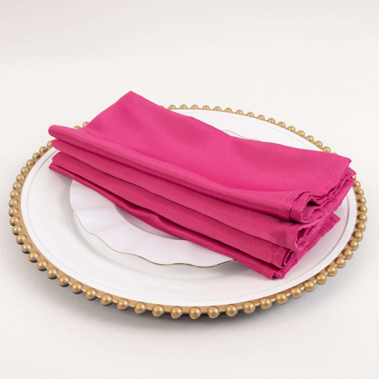Fuchsia satin napkins stacked on a decorative plate.
