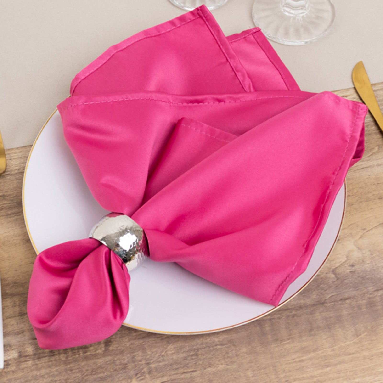 Fuchsia satin napkins elegantly folded on a plate with a silver napkin ring.