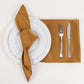 Gold satin napkin on a white plate with cutlery.