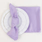 Lavender lilac satin napkins on a white plate with a matching napkin.