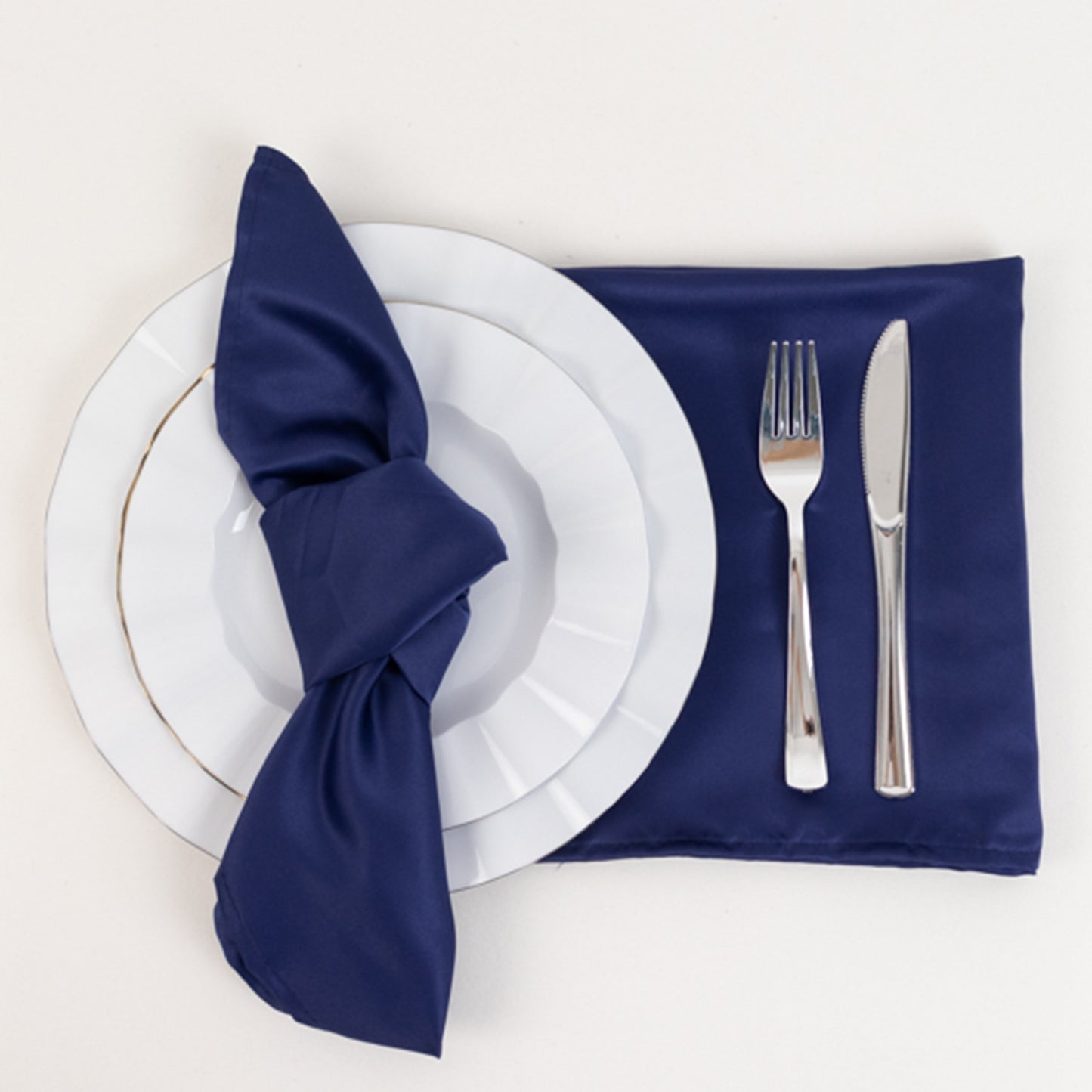 Navy blue satin napkins on a table setting with white plates and silver cutlery.