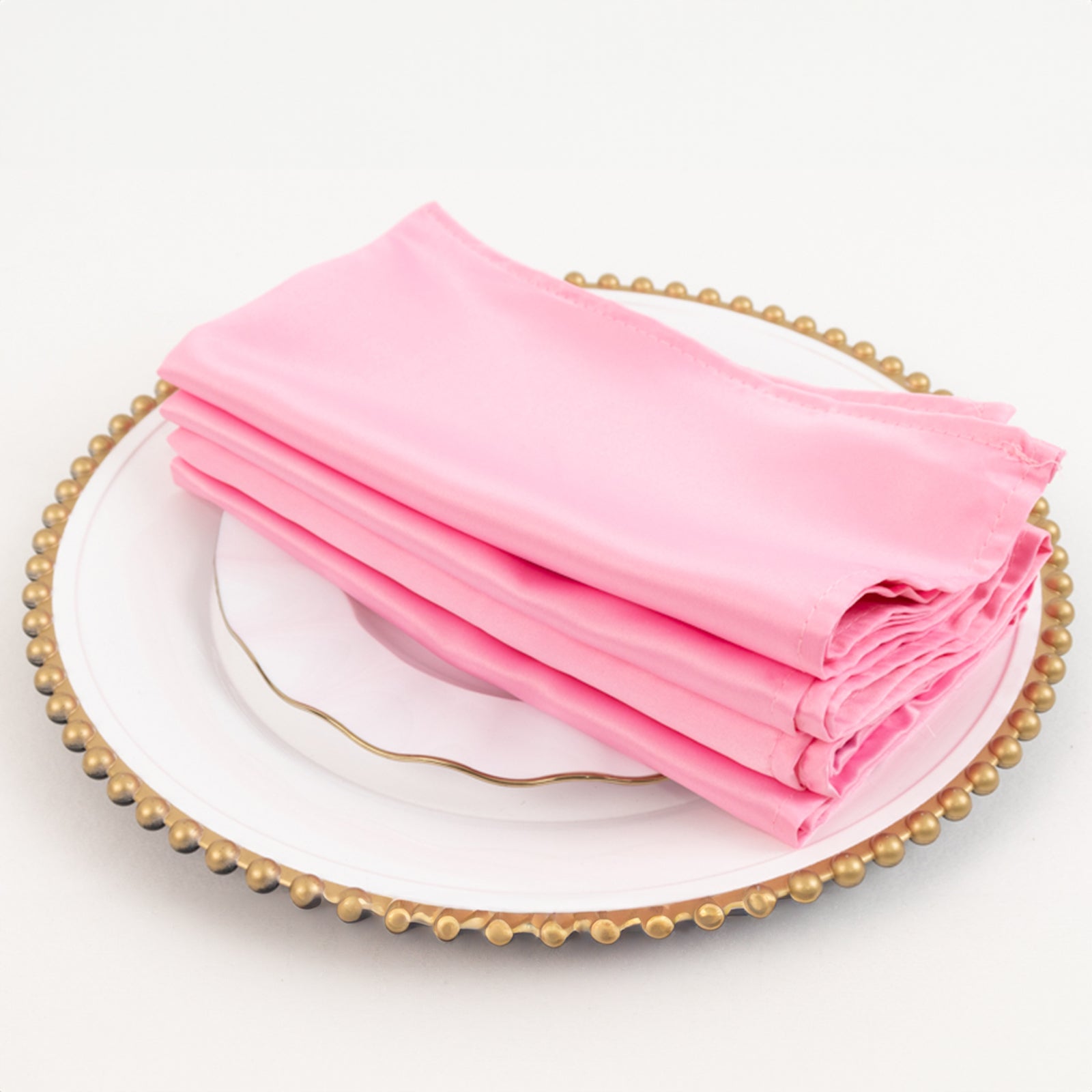 Pink satin napkins stacked on a decorative plate.