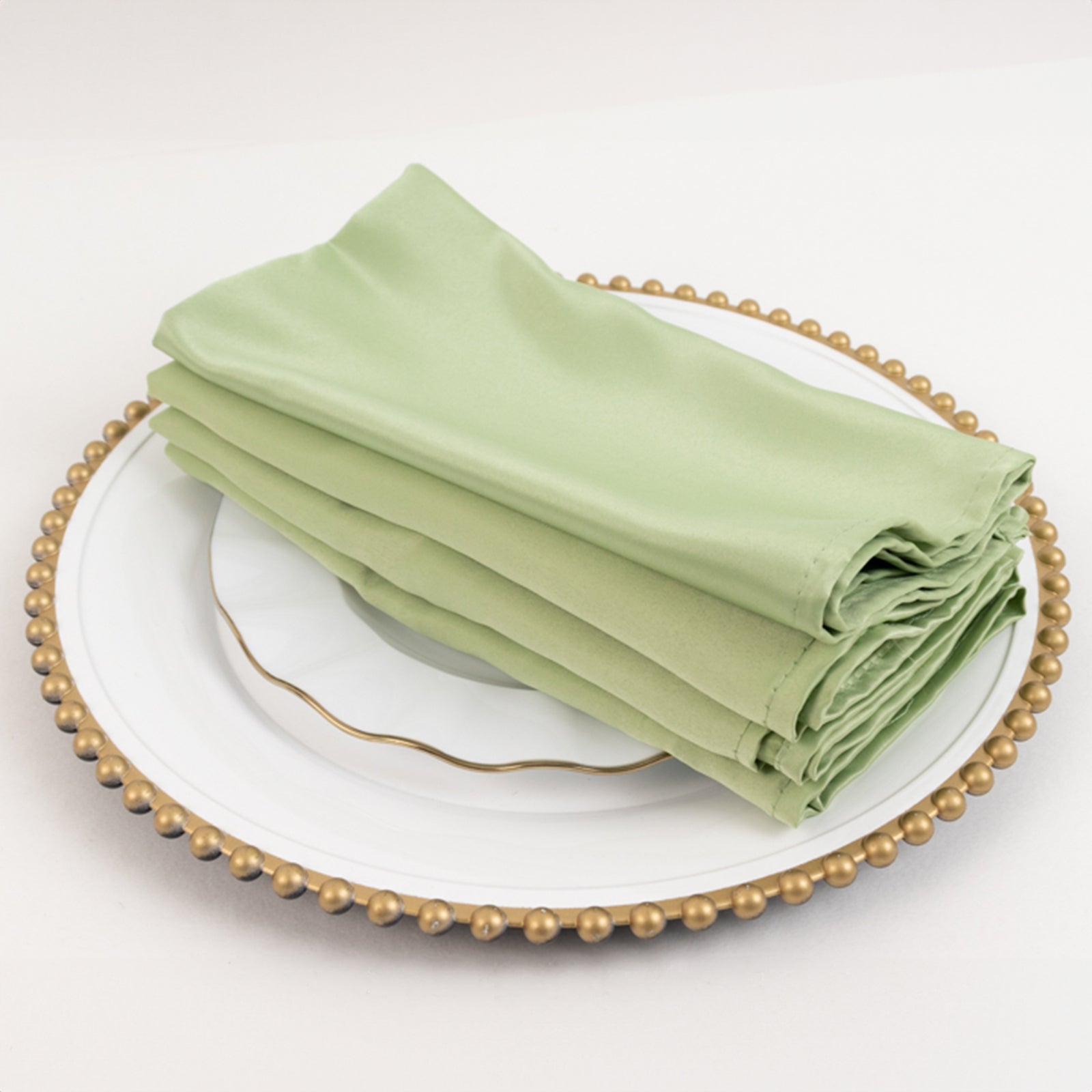 Sage green satin napkins stacked on a decorative plate.