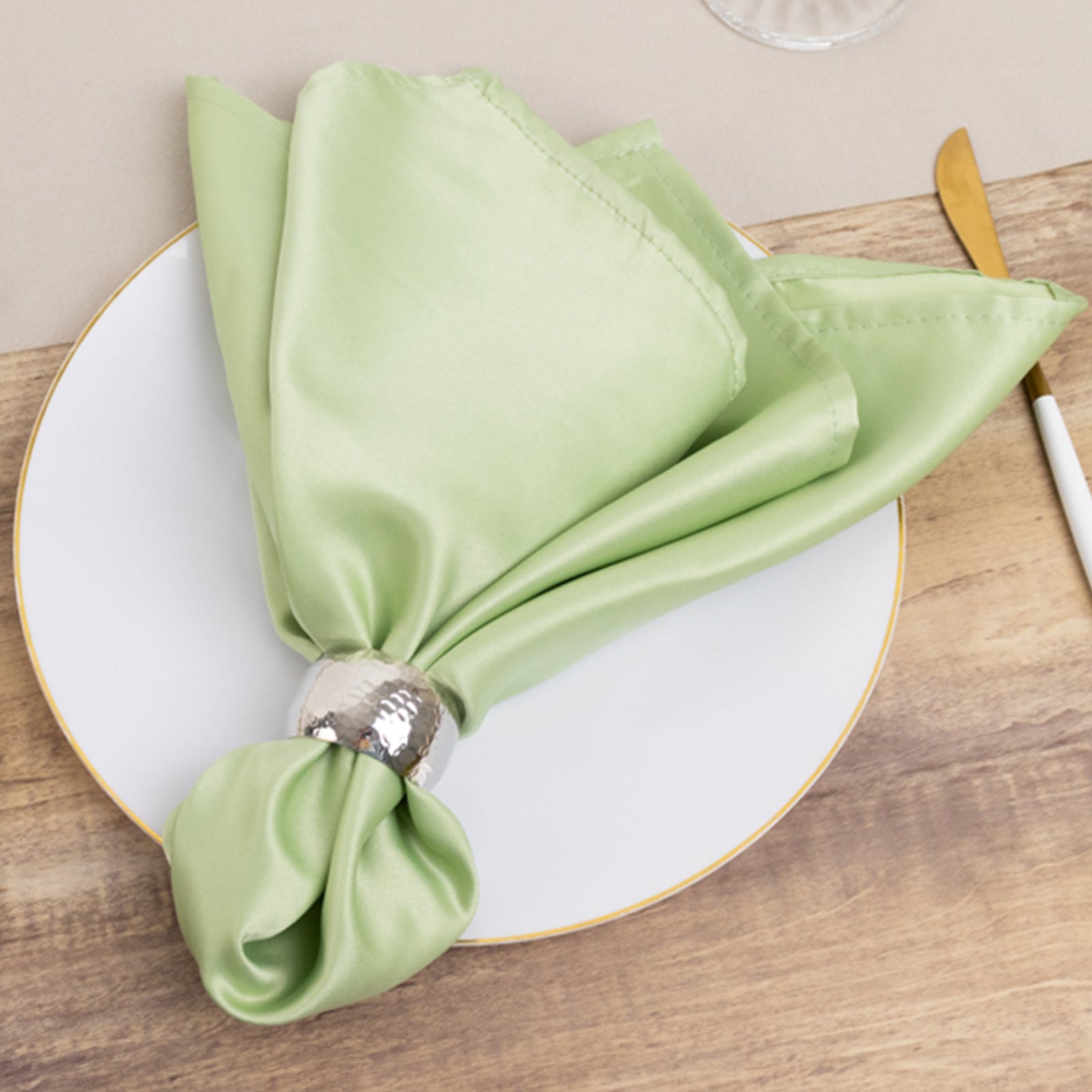 Sage green satin napkin elegantly folded on a white plate.