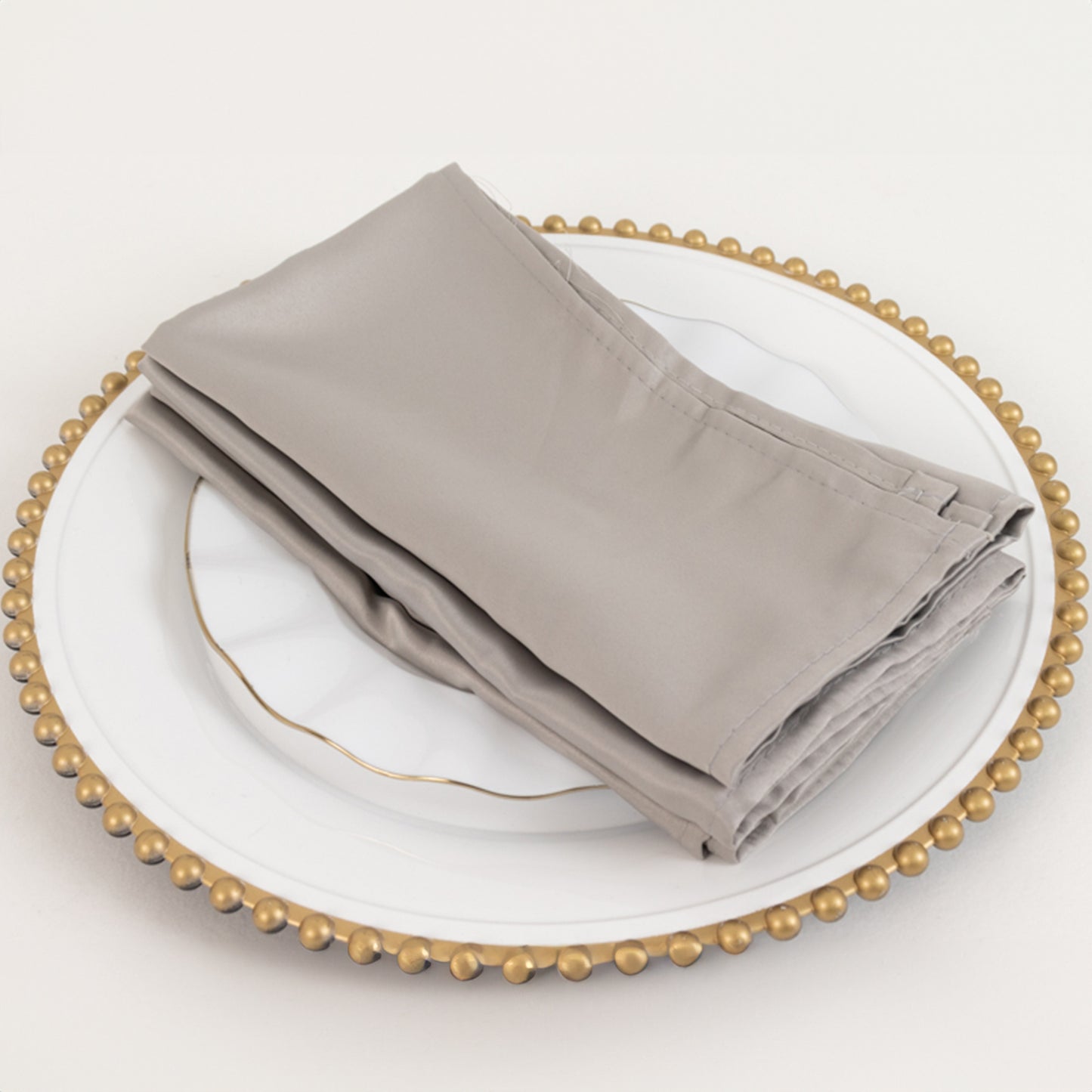 Silver satin napkins on a decorative plate.