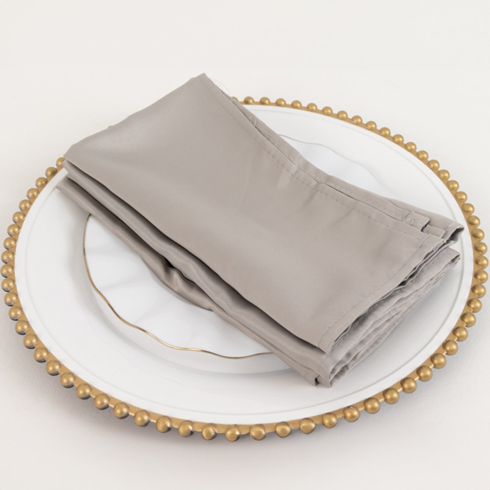 Silver satin napkins on a decorative plate.