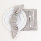 Silver satin napkins on a table setting with white plate and silverware.