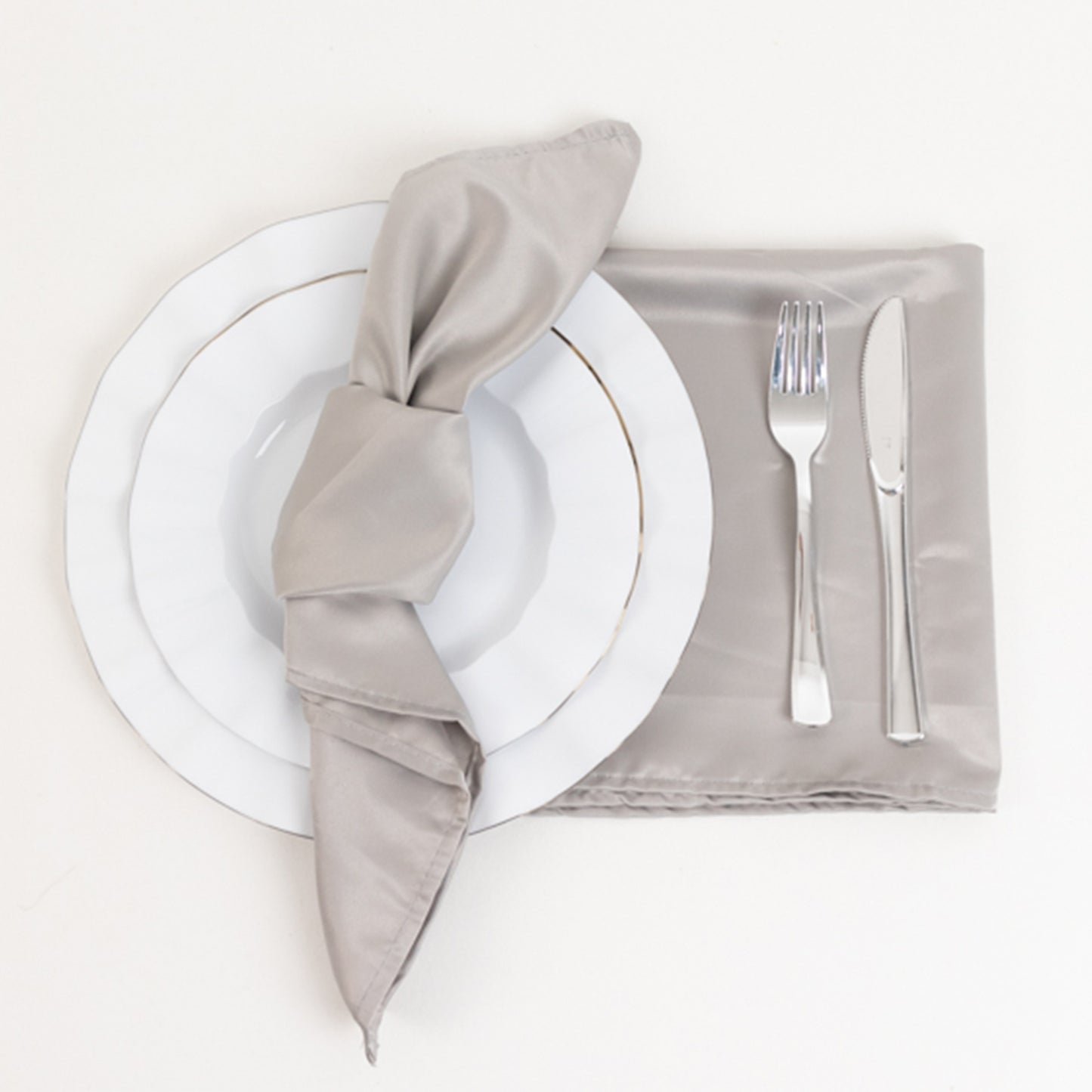Silver satin napkins on a table setting with white plate and silverware.