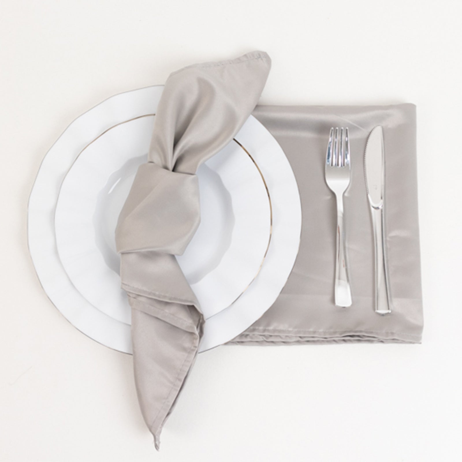 Silver satin napkins on a table setting with white plate and silverware.