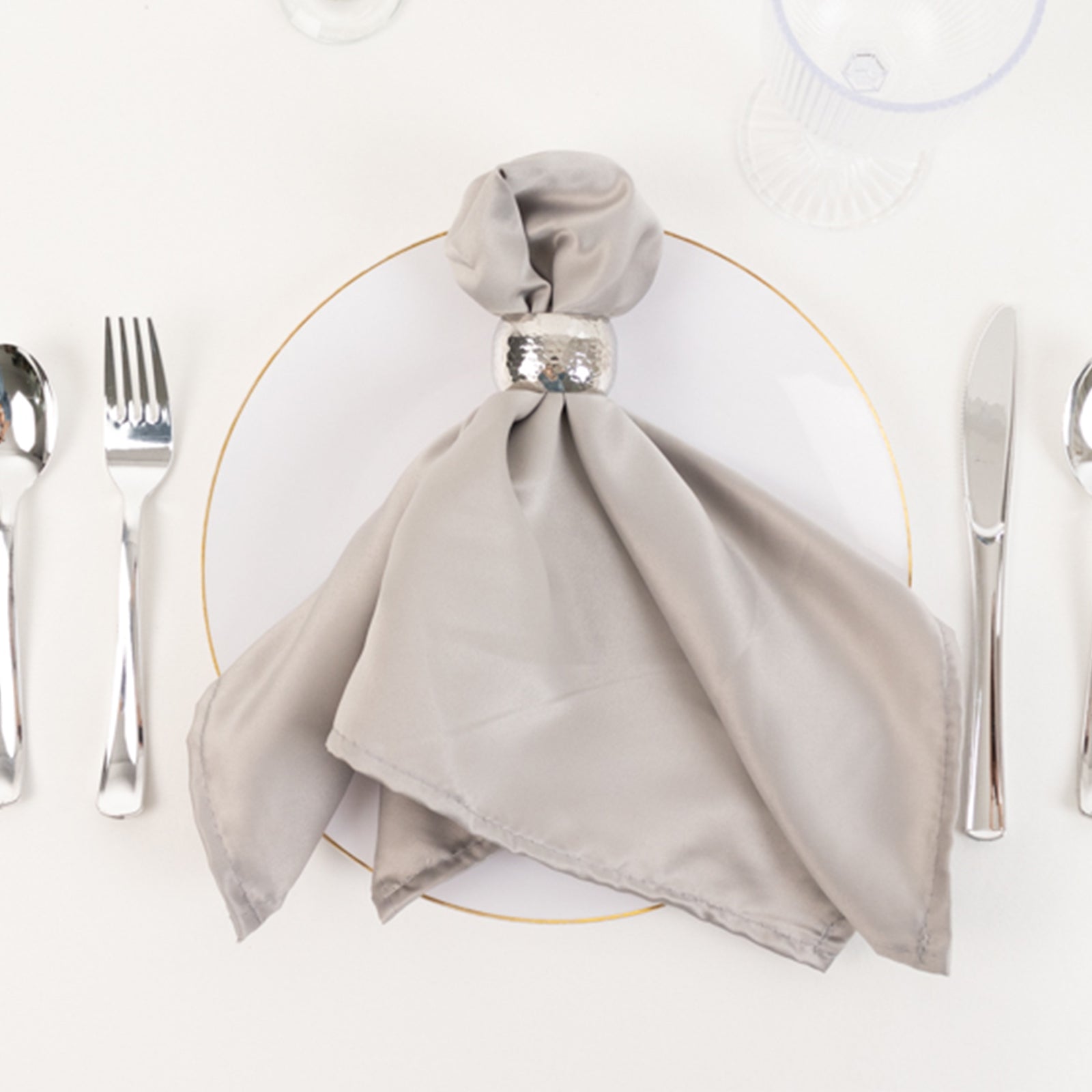 Silver satin napkin on a white plate, elegantly styled for dining.