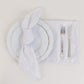 White satin napkins set on a table with a plate and cutlery.