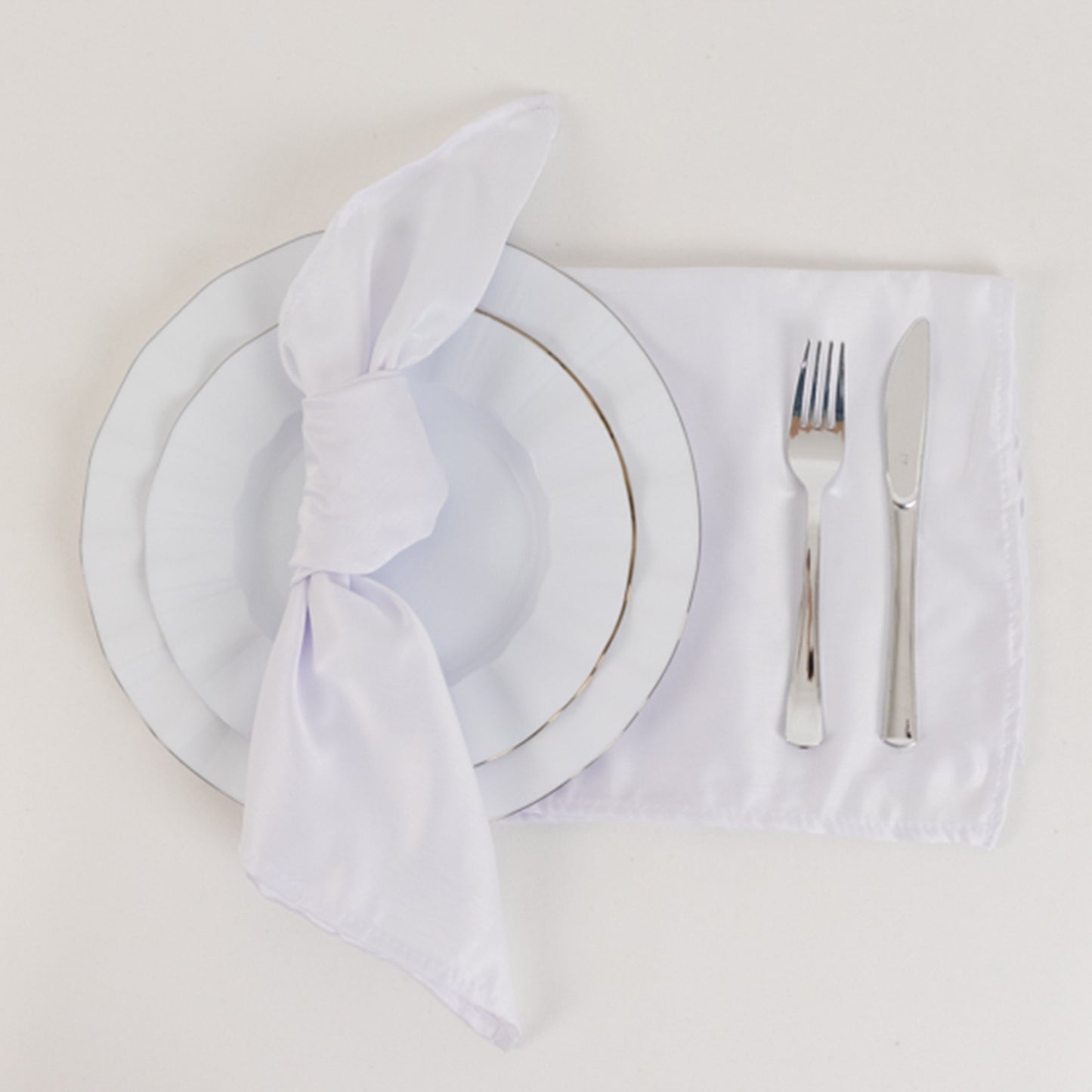 White satin napkins set on a table with a plate and cutlery.