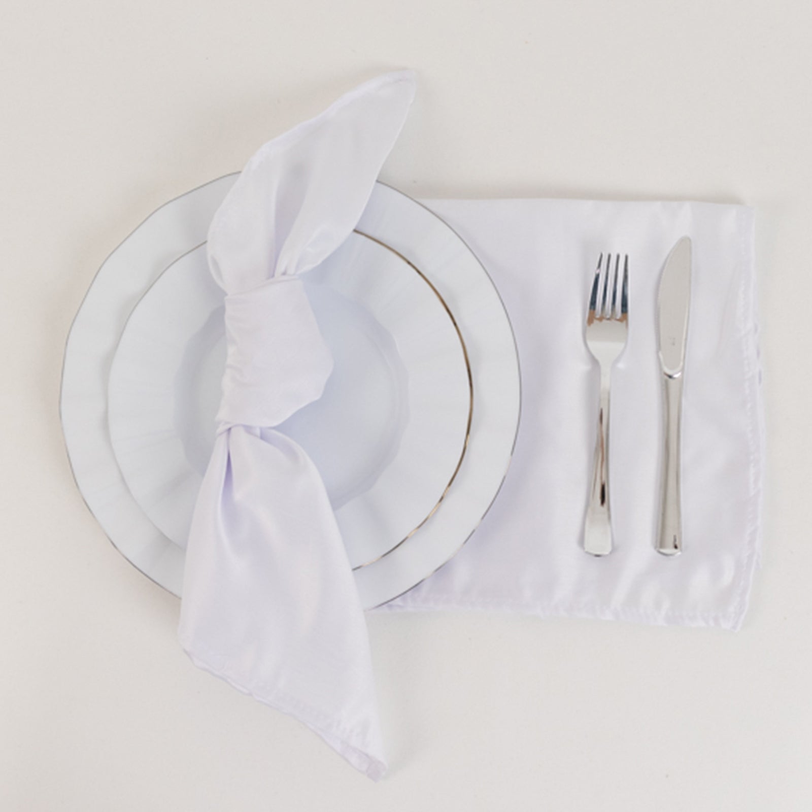 White satin napkins set on a table with a plate and cutlery.