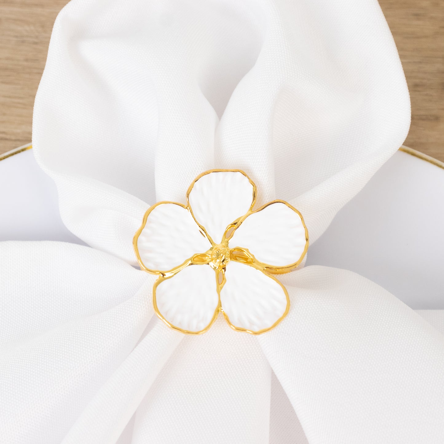 White and gold floral napkin ring on a white napkin.