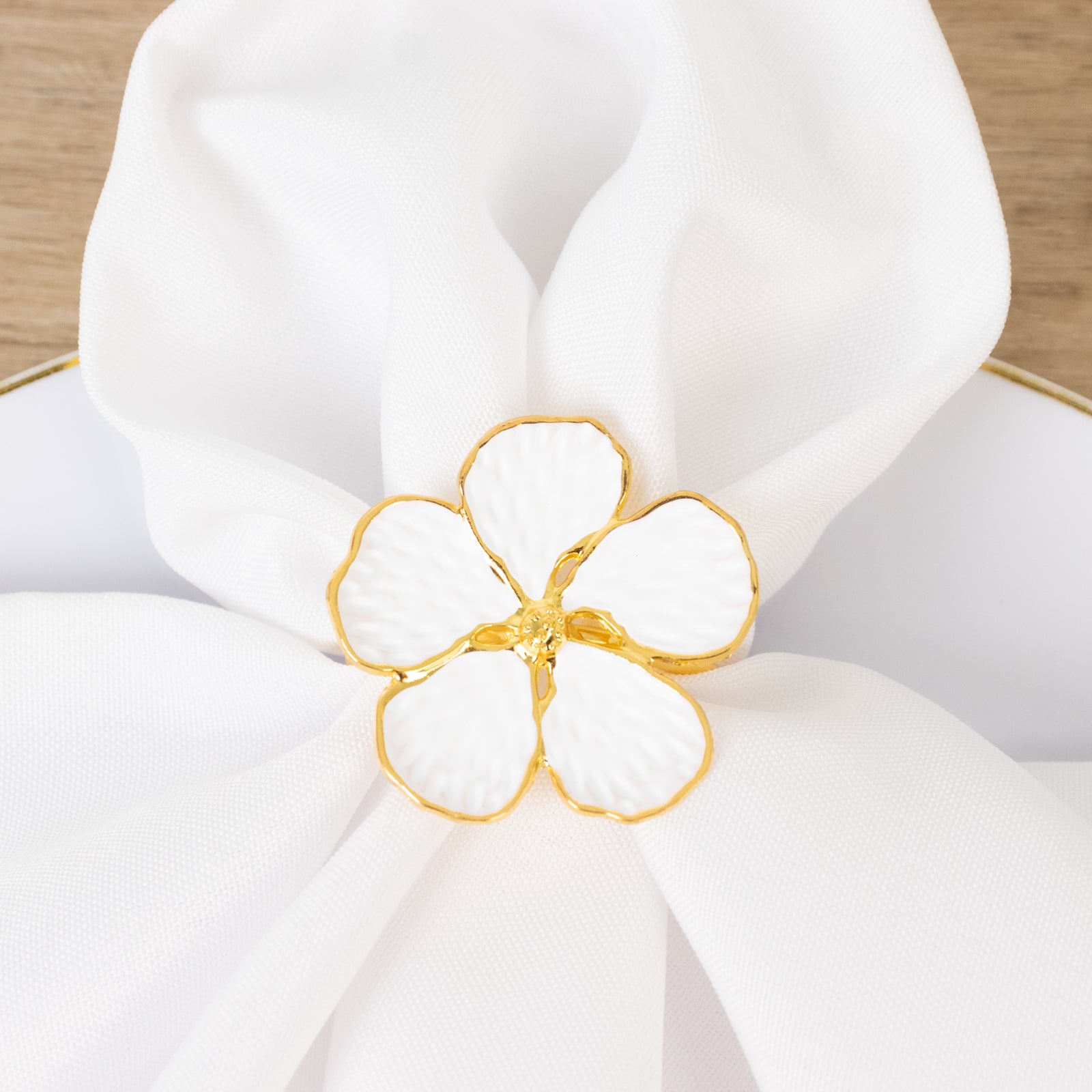 White and gold floral napkin ring on a white napkin.