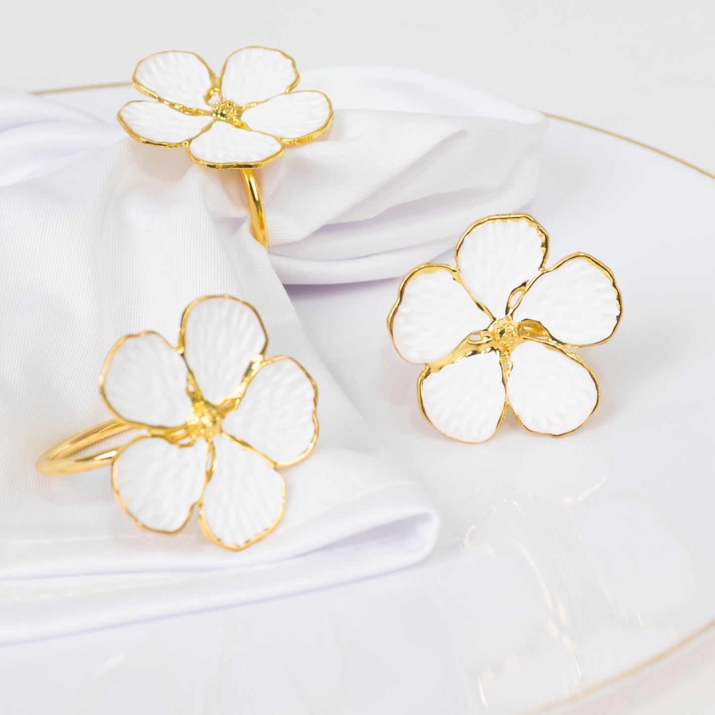 White and gold floral napkin rings on a white napkin.
