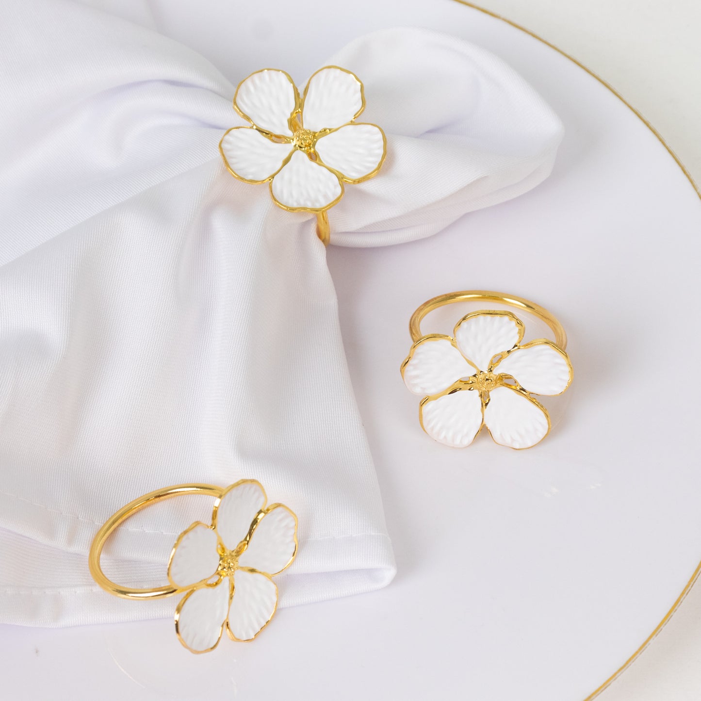 White and gold floral napkin rings on a white napkin.