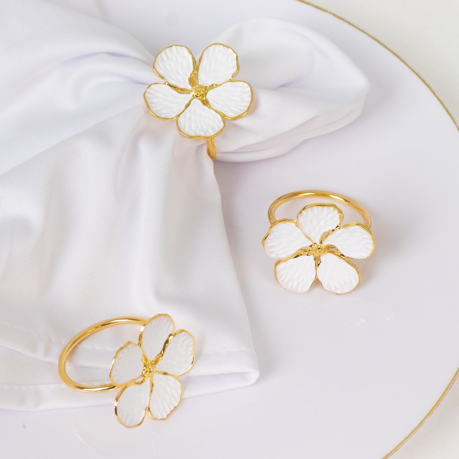 White and gold floral napkin rings on a white napkin.