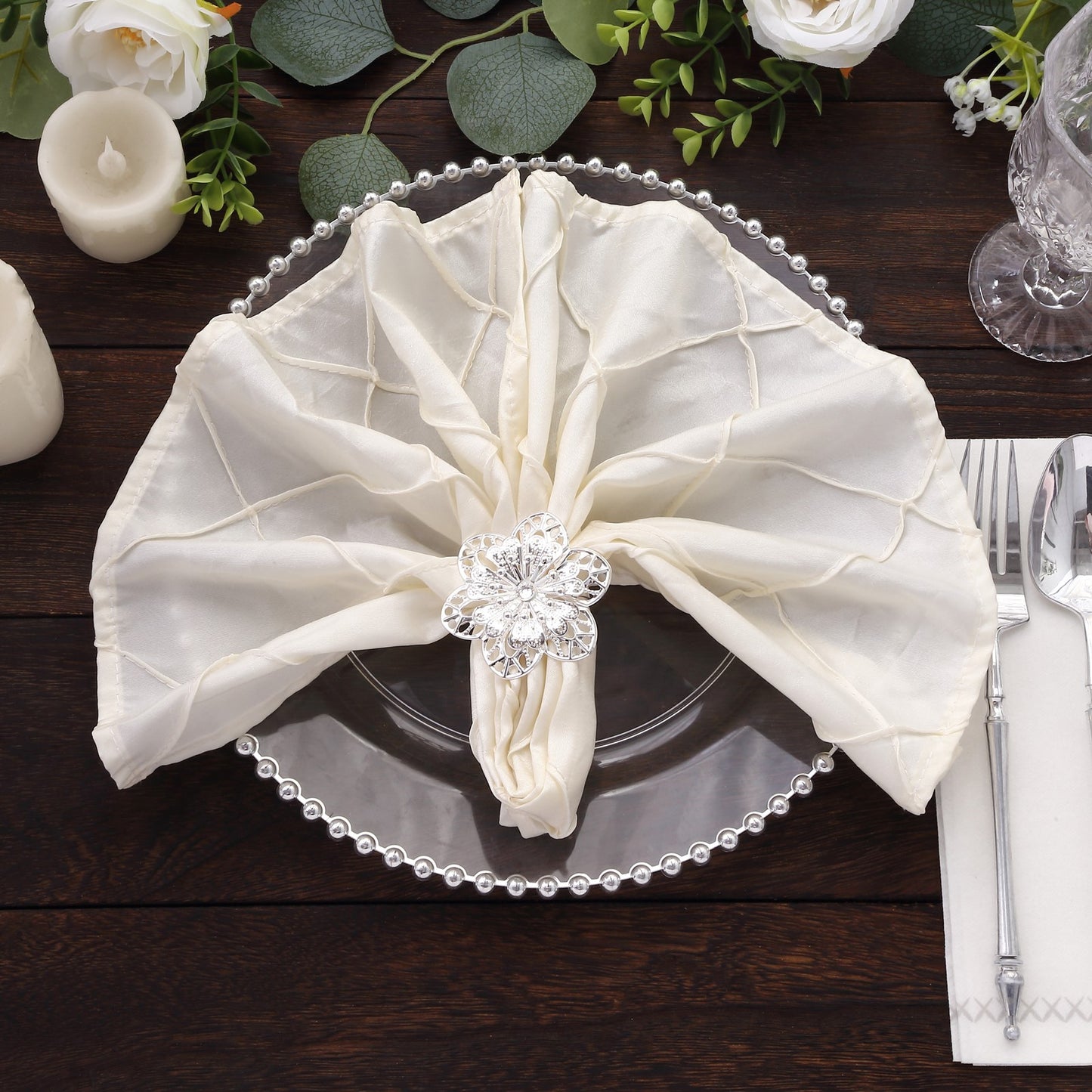 Silver metal hollow flower napkin rings on a cream napkin.