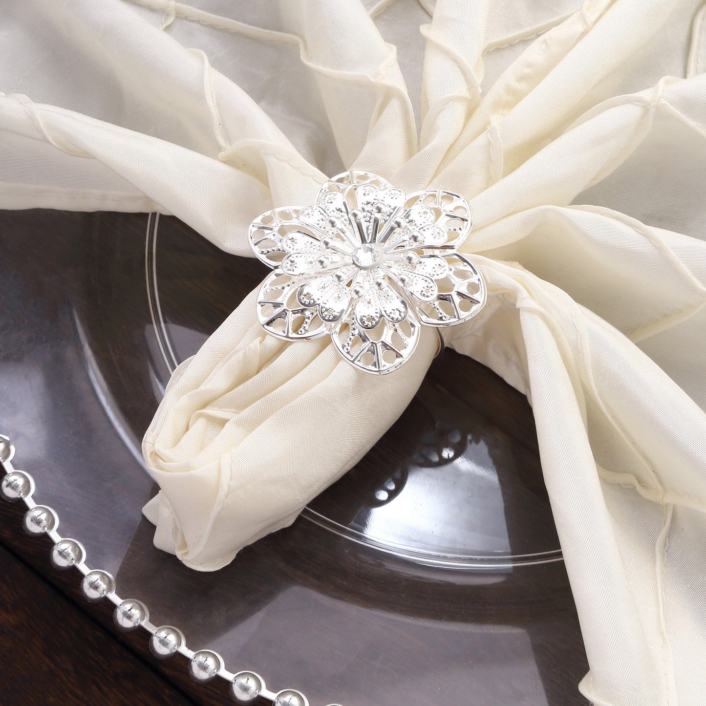 Silver metal hollow sun flower napkin rings on a cream napkin.