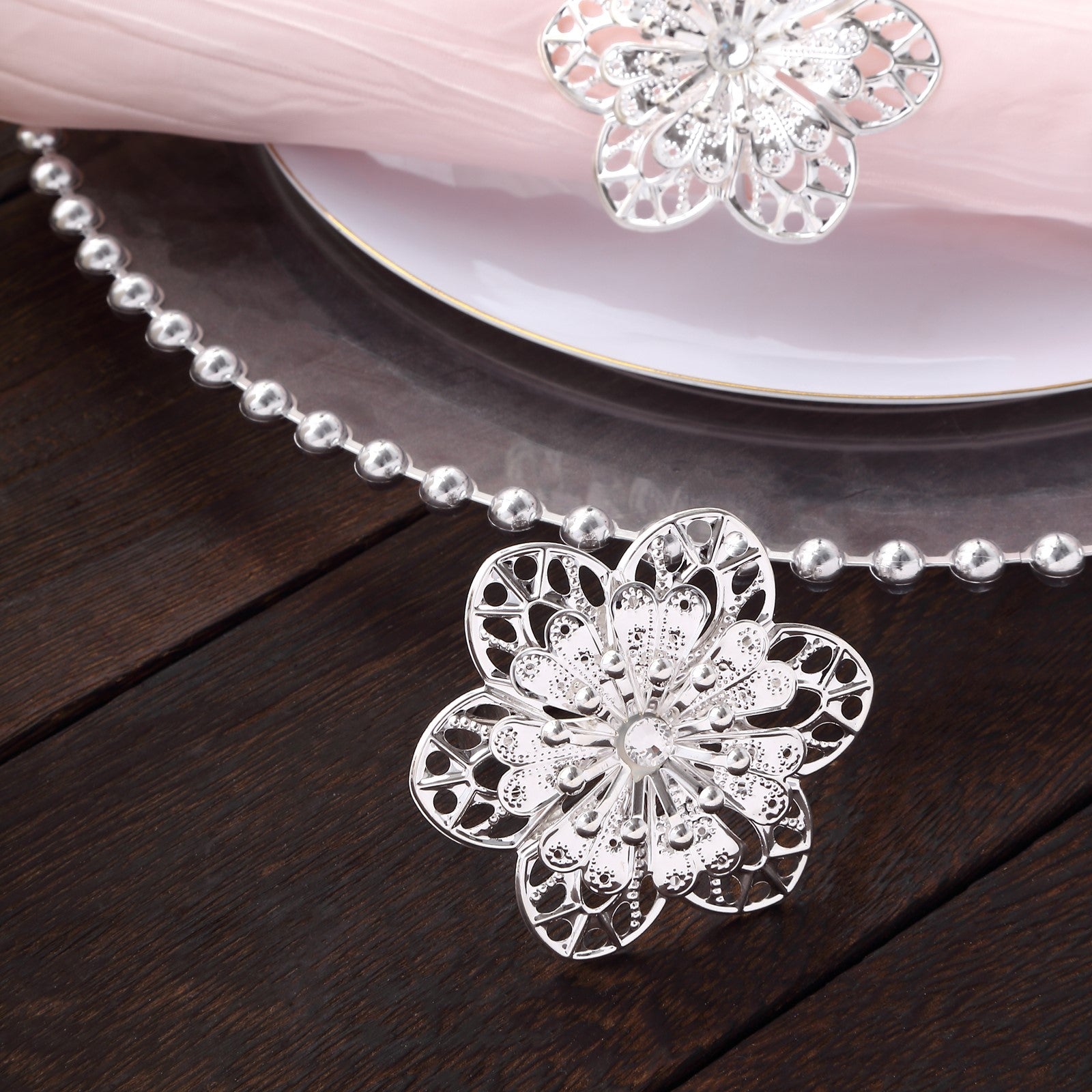 Silver metal hollow sun flower napkin rings on a wooden table.