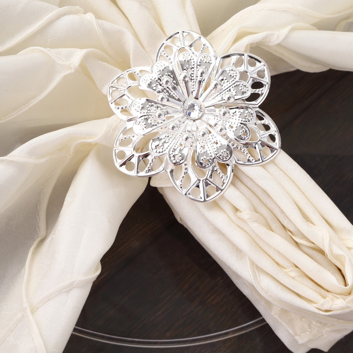 Silver metal hollow flower napkin ring on a cream napkin.