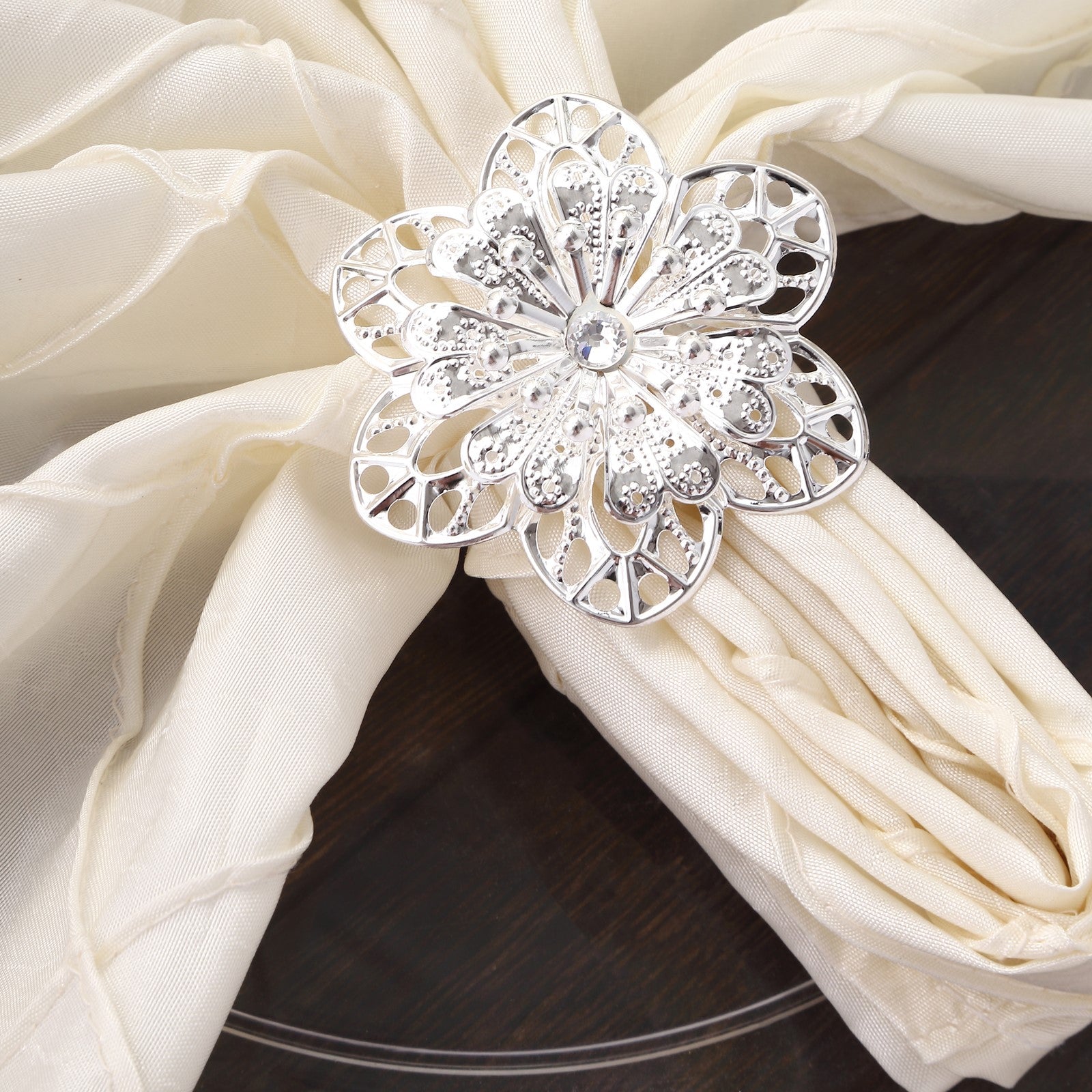 Silver metal hollow flower napkin ring on a cream napkin.