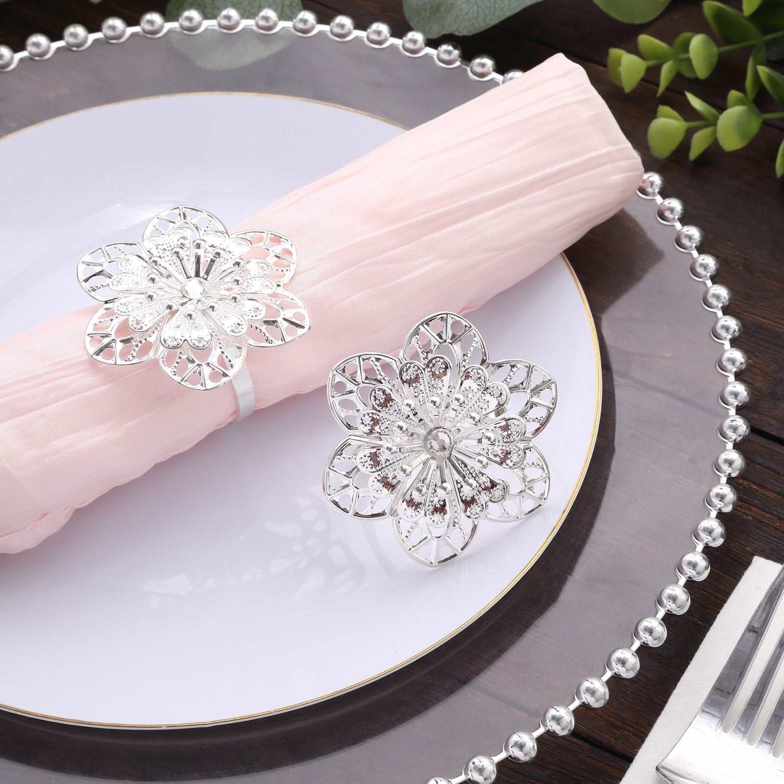 Silver metal hollow sun flower napkin rings on a pink napkin.