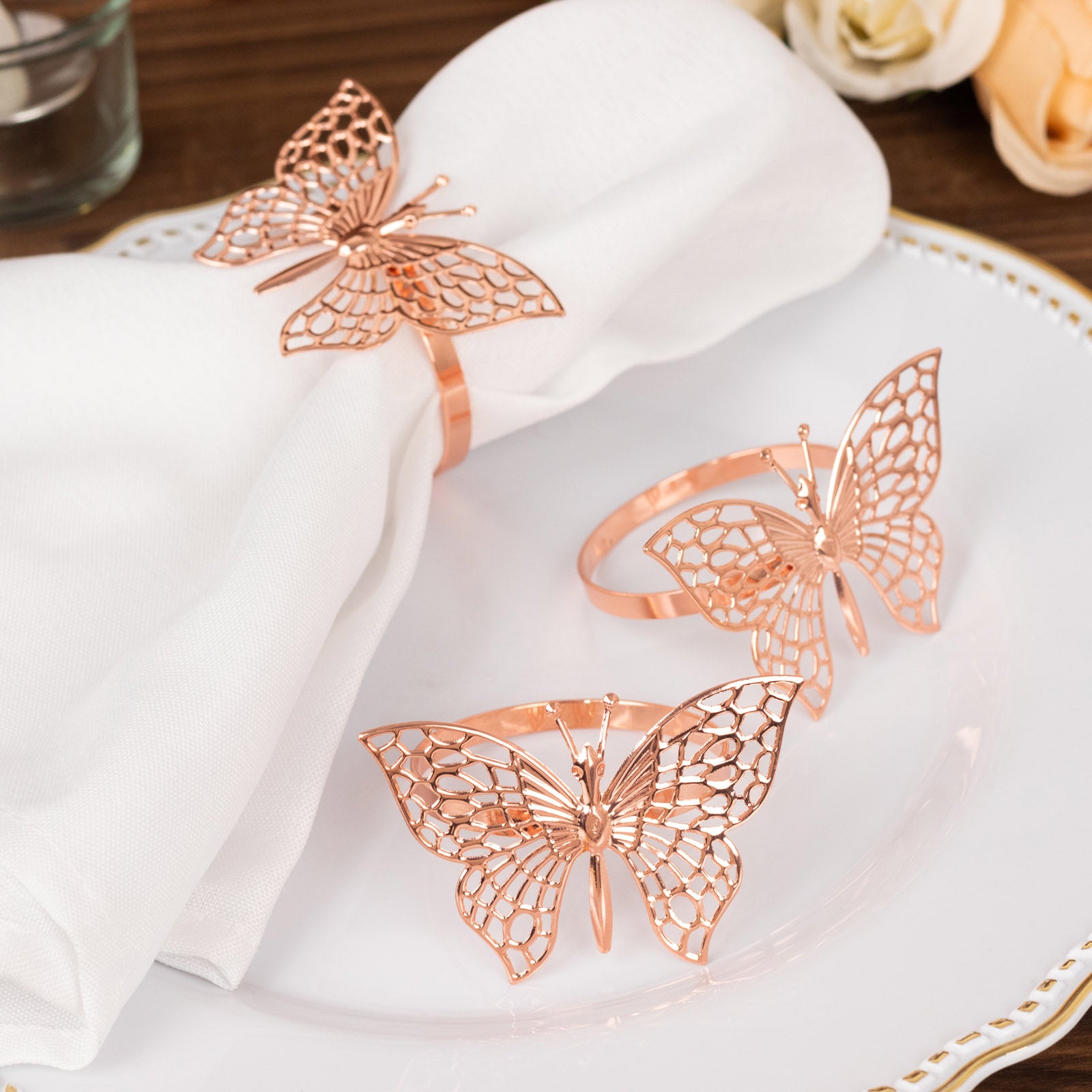 Rose gold metal butterfly napkin rings on white cloth napkins.