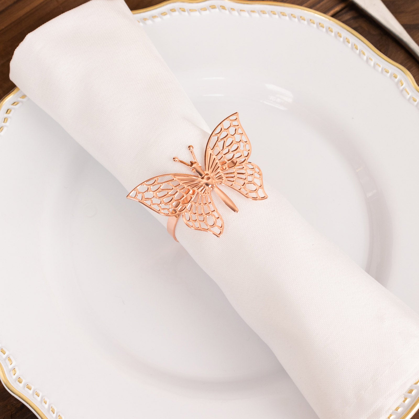 Rose gold butterfly napkin ring on a white cloth napkin.