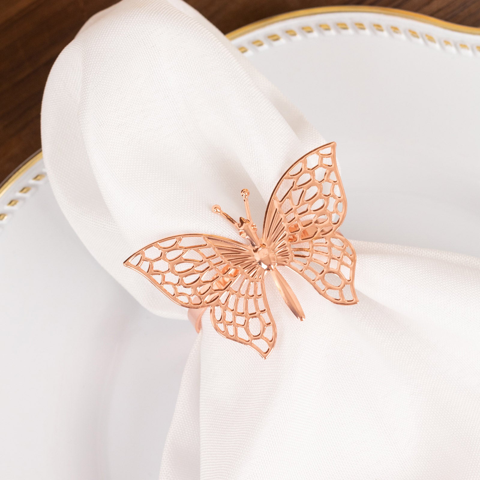 Rose gold butterfly napkin ring holding a white cloth napkin.
