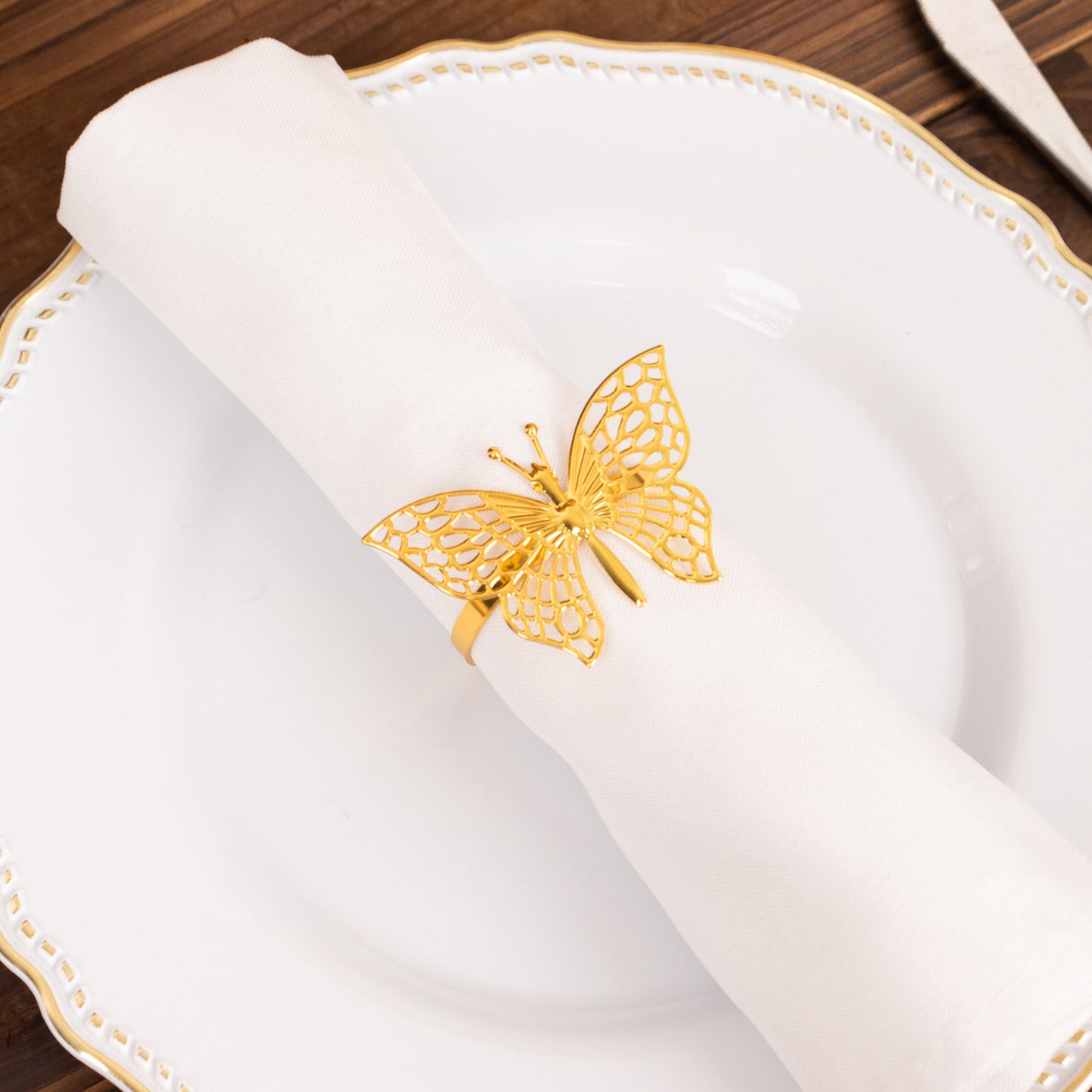 Gold butterfly napkin ring holding a white cloth napkin on a decorative plate.