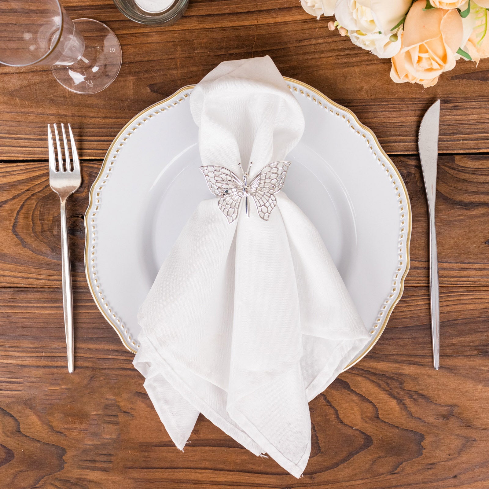 Silver butterfly napkin rings on a white plate with a cloth napkin.