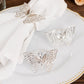 Silver metal butterfly napkin rings on a white cloth napkin.