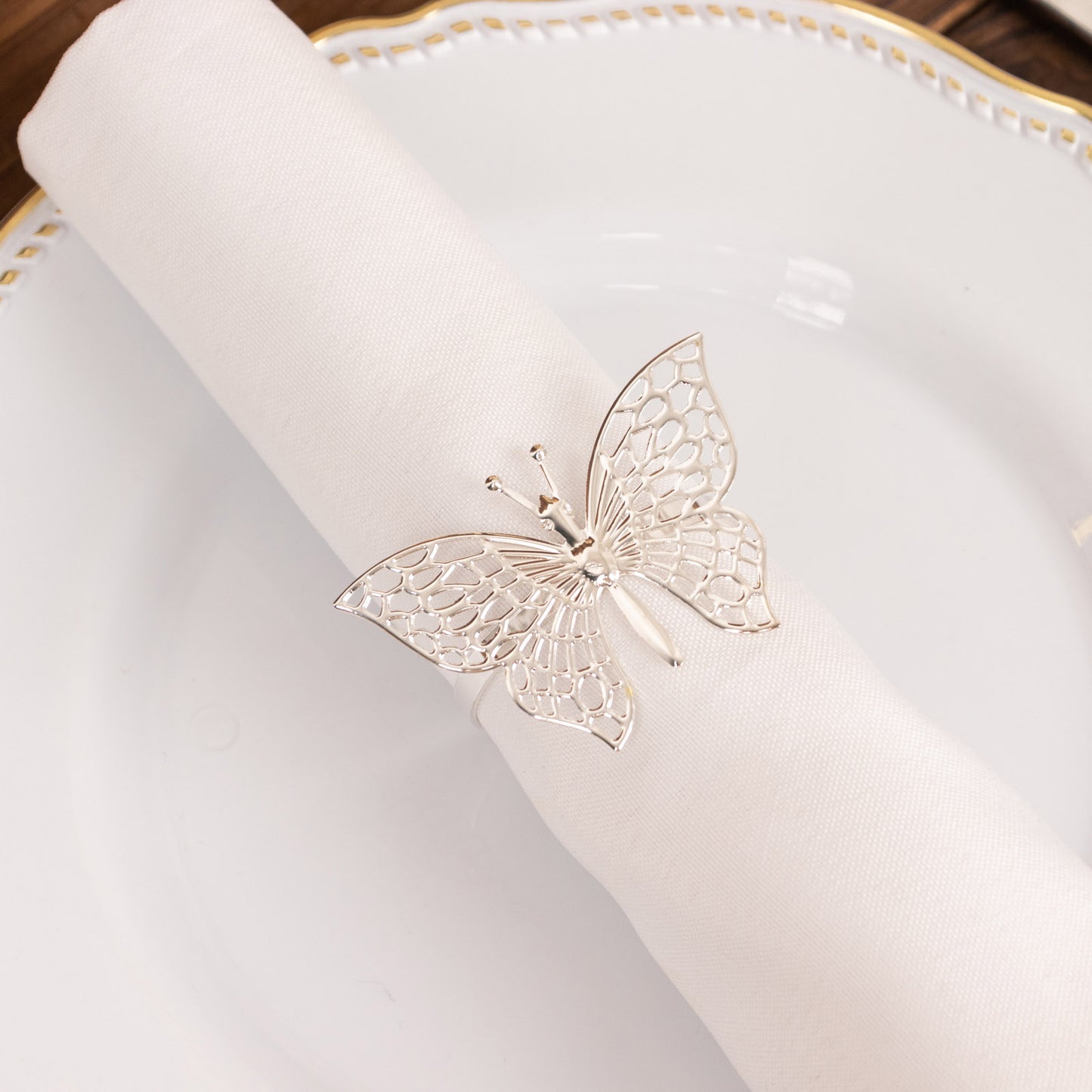 Silver metal butterfly napkin rings on white cloth napkin.