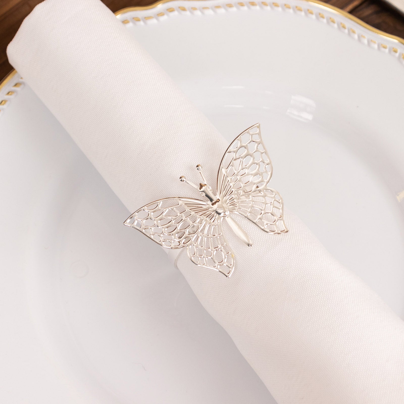 Silver metal butterfly napkin rings on white cloth napkin.