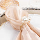 White pearl and gold metal napkin holder on a satin napkin.