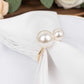 White pearl and gold metal napkin holder on a white napkin.
