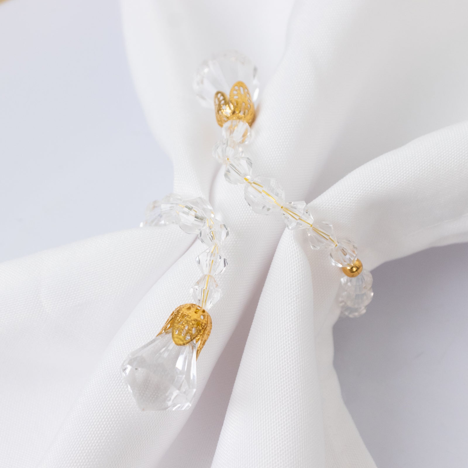 Clear crystal beaded napkin rings with gold accents on a white napkin.