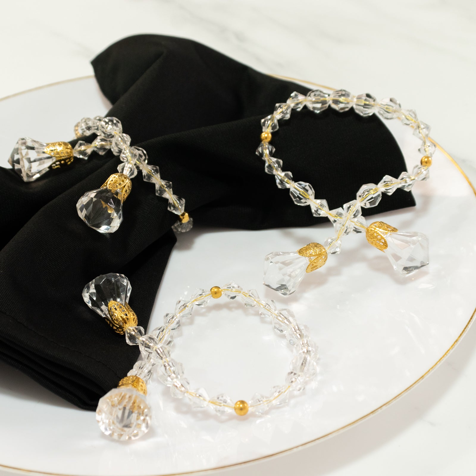 Clear crystal beaded napkin rings with gold accents on a black napkin.