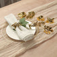 Glossy gold metal leaf napkin rings on a table setting with a napkin.