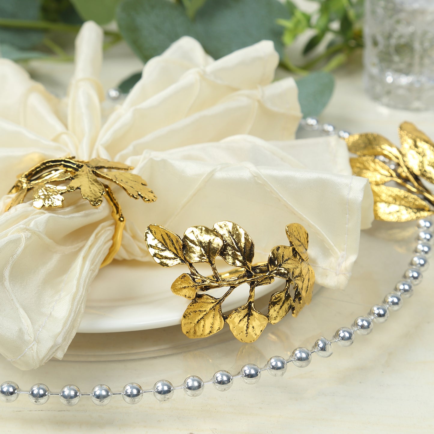 Glossy gold metal leaf napkin rings with vintage herb design.
