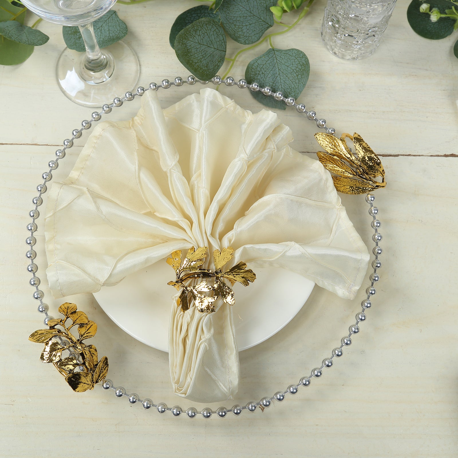 Glossy gold metal leaf napkin rings with vintage herb design on a cream napkin.