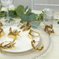 Glossy gold metal leaf napkin rings on a table setting.
