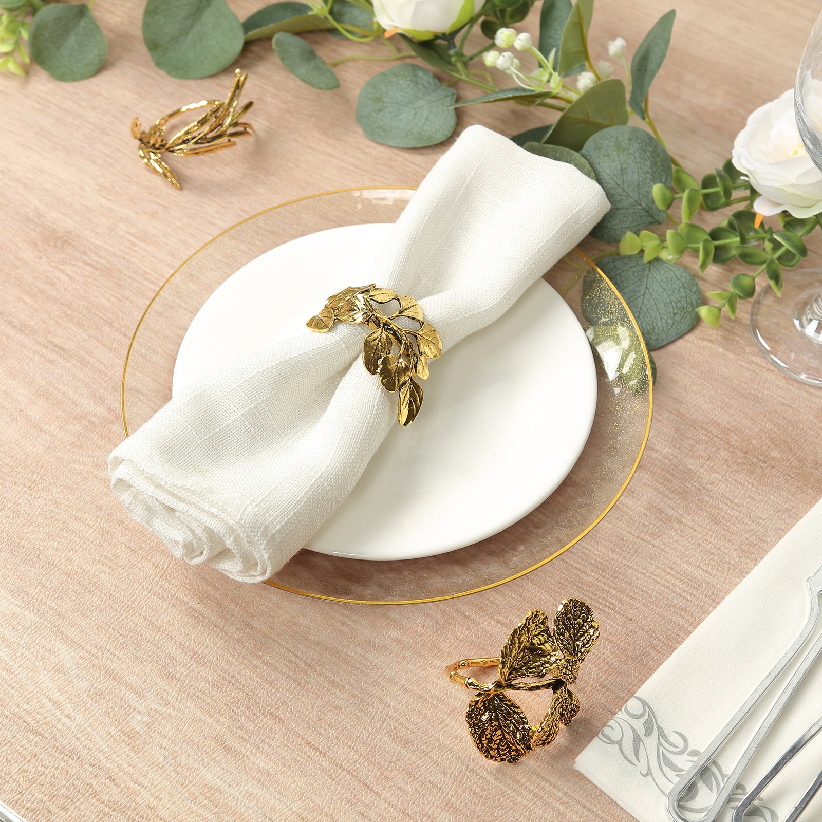 Glossy gold metal leaf napkin rings on a table setting with white napkin.