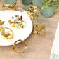 Glossy gold metal leaf napkin rings on a plate with greenery.
