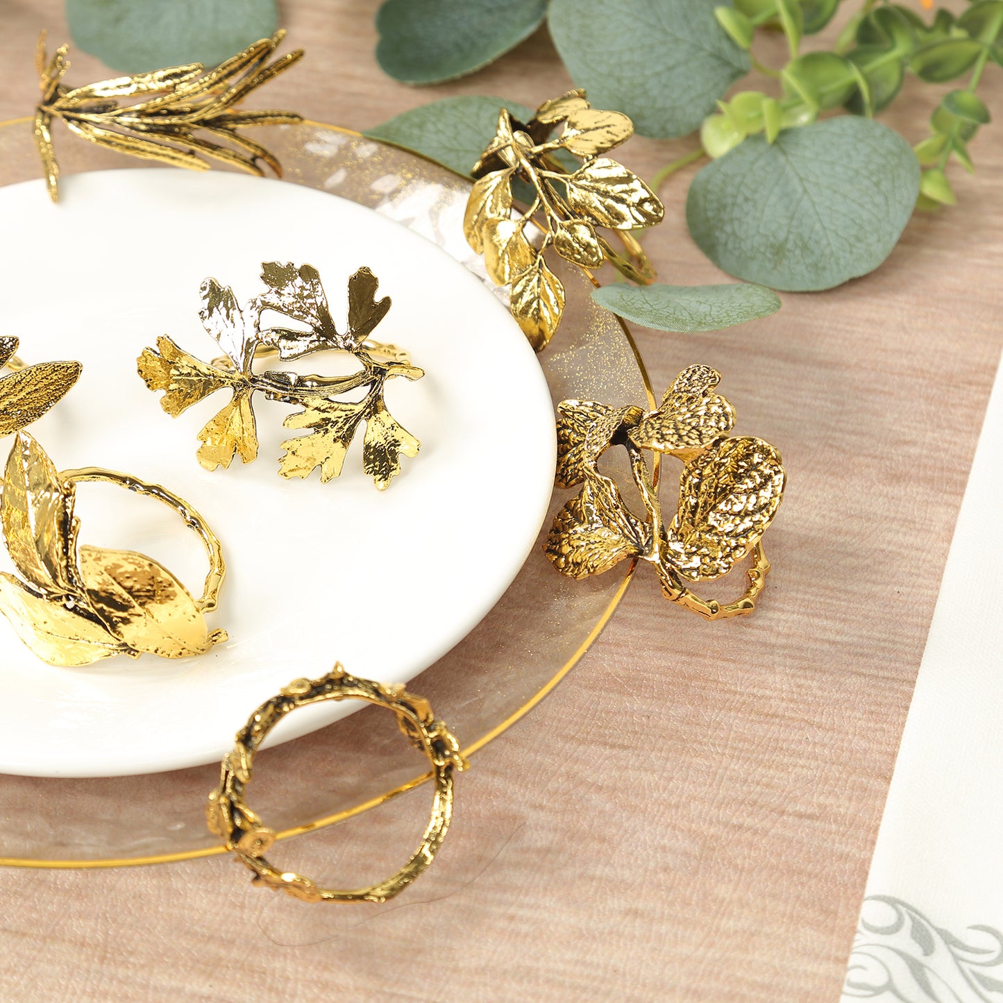 Glossy gold metal leaf napkin rings on a plate with greenery.