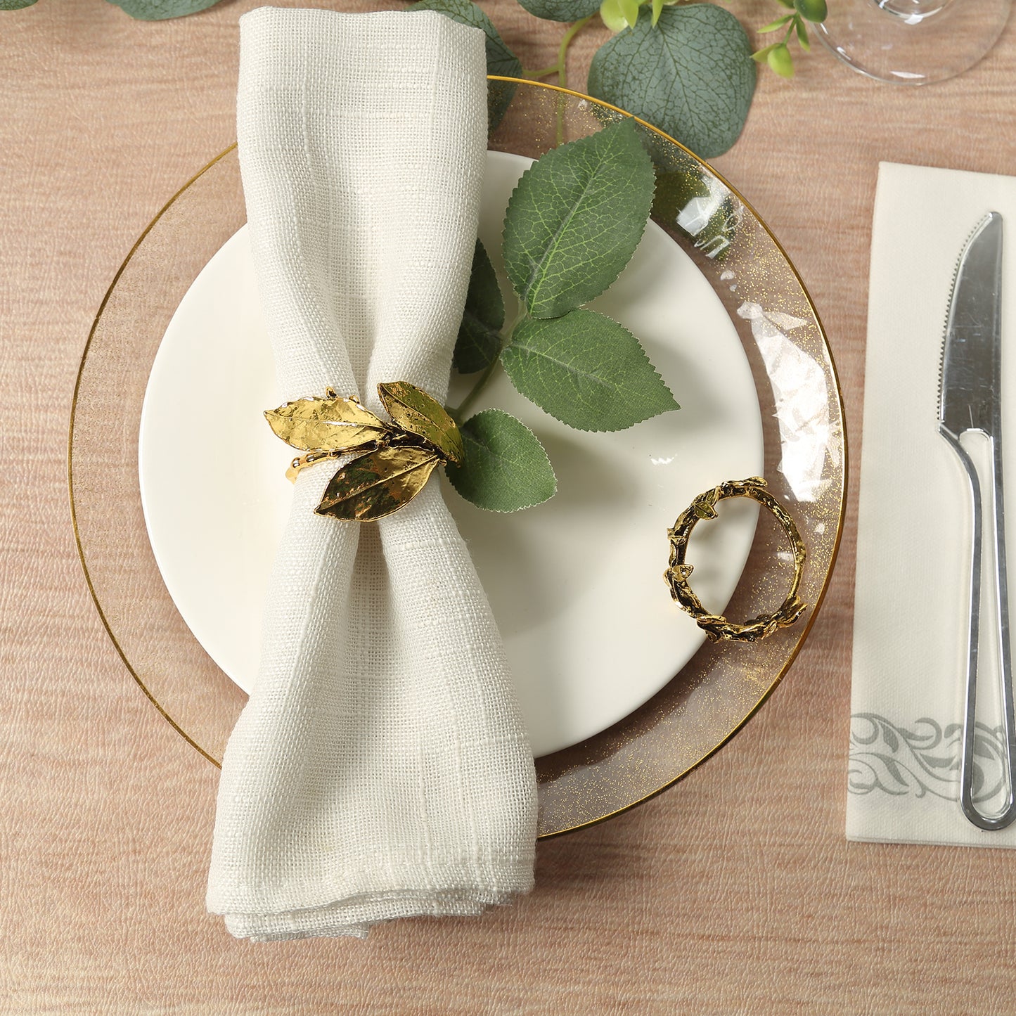 Glossy gold metal leaf napkin ring with vintage herb design on a table setting.