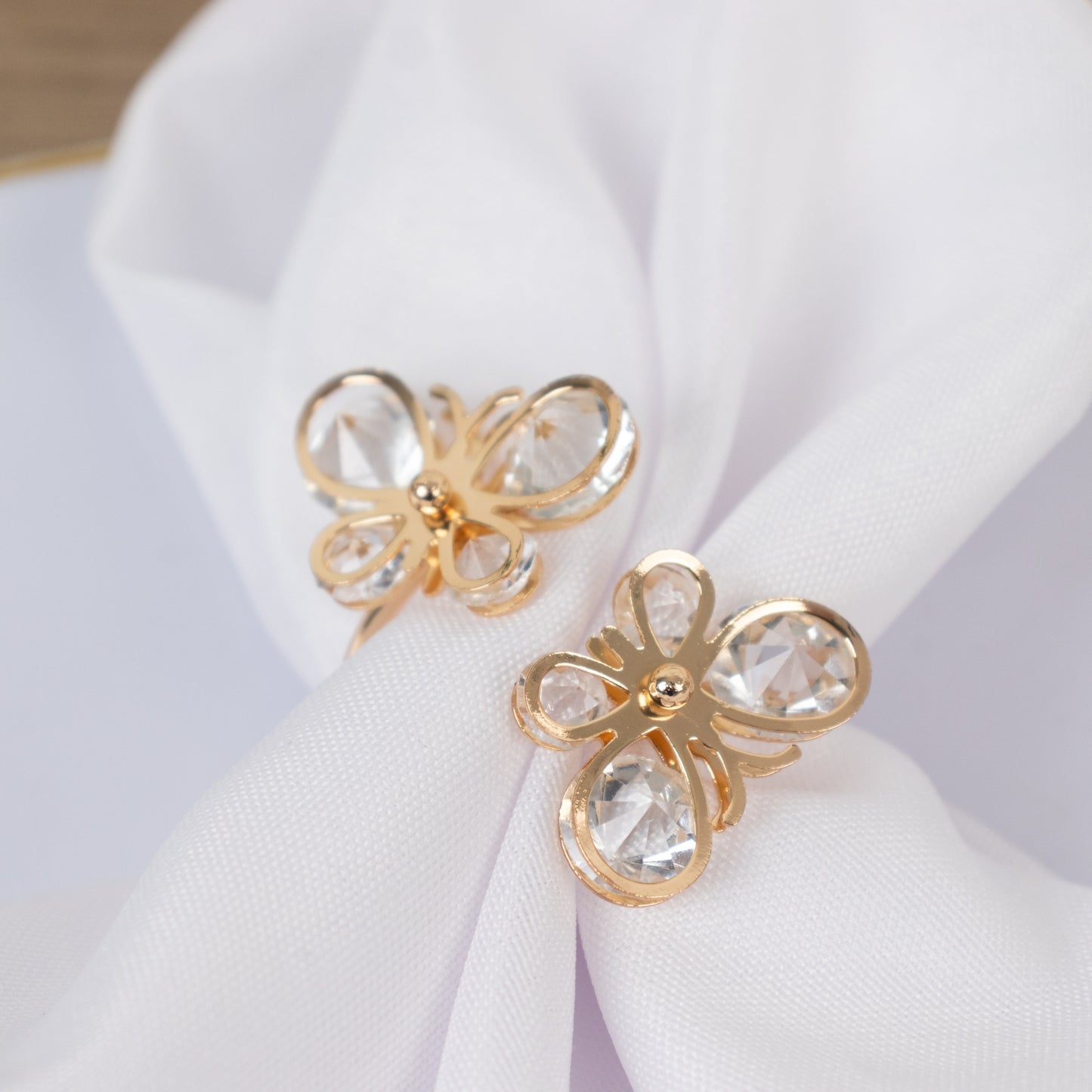 Gold butterfly napkin holders with crystal accents on white fabric.
